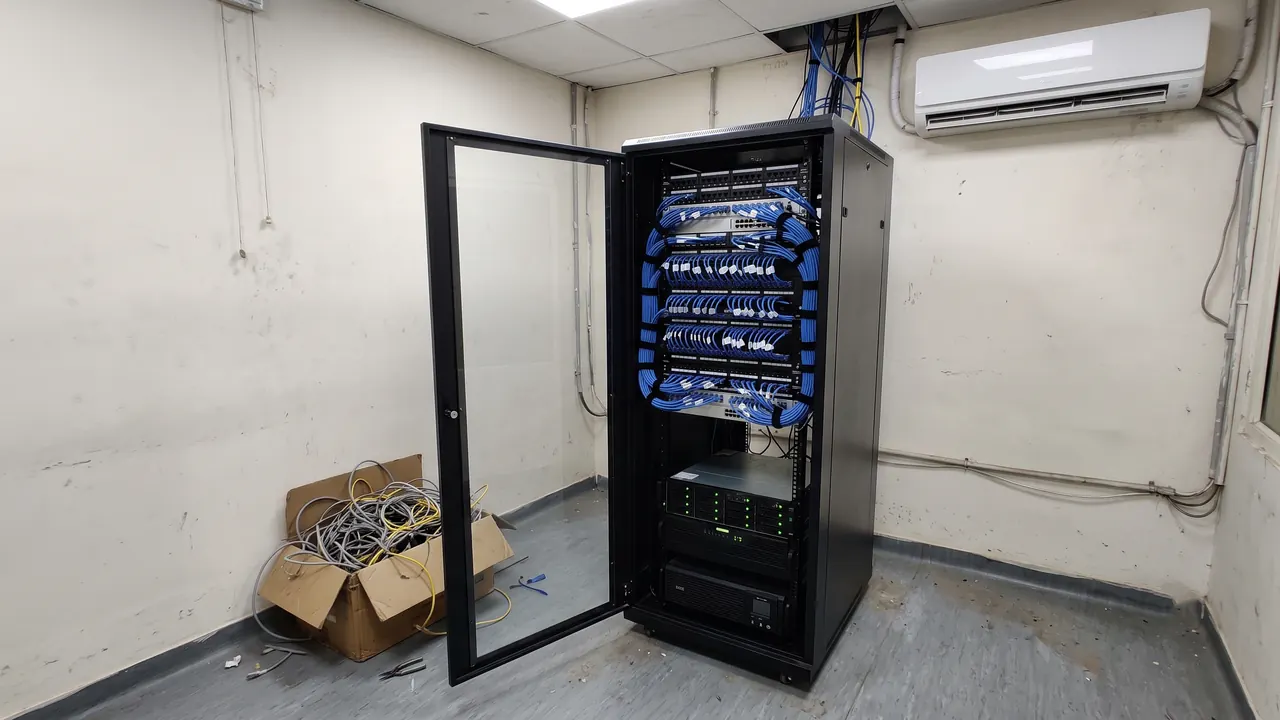 Rebuilt floor-standing network rack with dressed blue patch cords, next to a carton of removed old cables